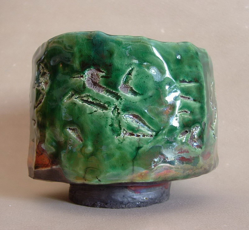 Tazza raku in ceramica verde smaltata con dettagli naturali e irregolarità tipiche della tecnica raku, simbolo di bellezza imperfetta e naturale.